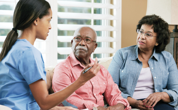 Female clinician speaks with elderly couple in their living room