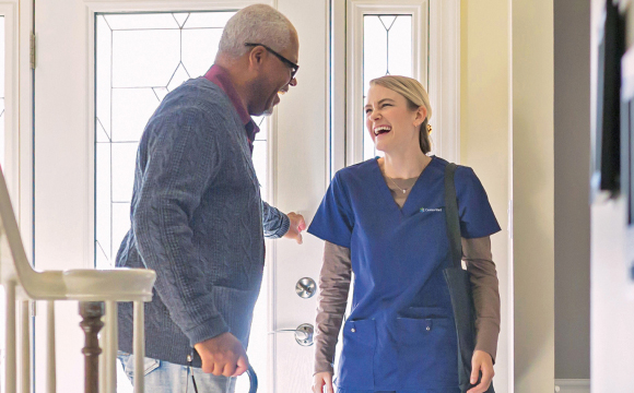 A smiling senior patient sits by his wife and recovers at home with the expert assistance of a skilled CenterWell nurse.